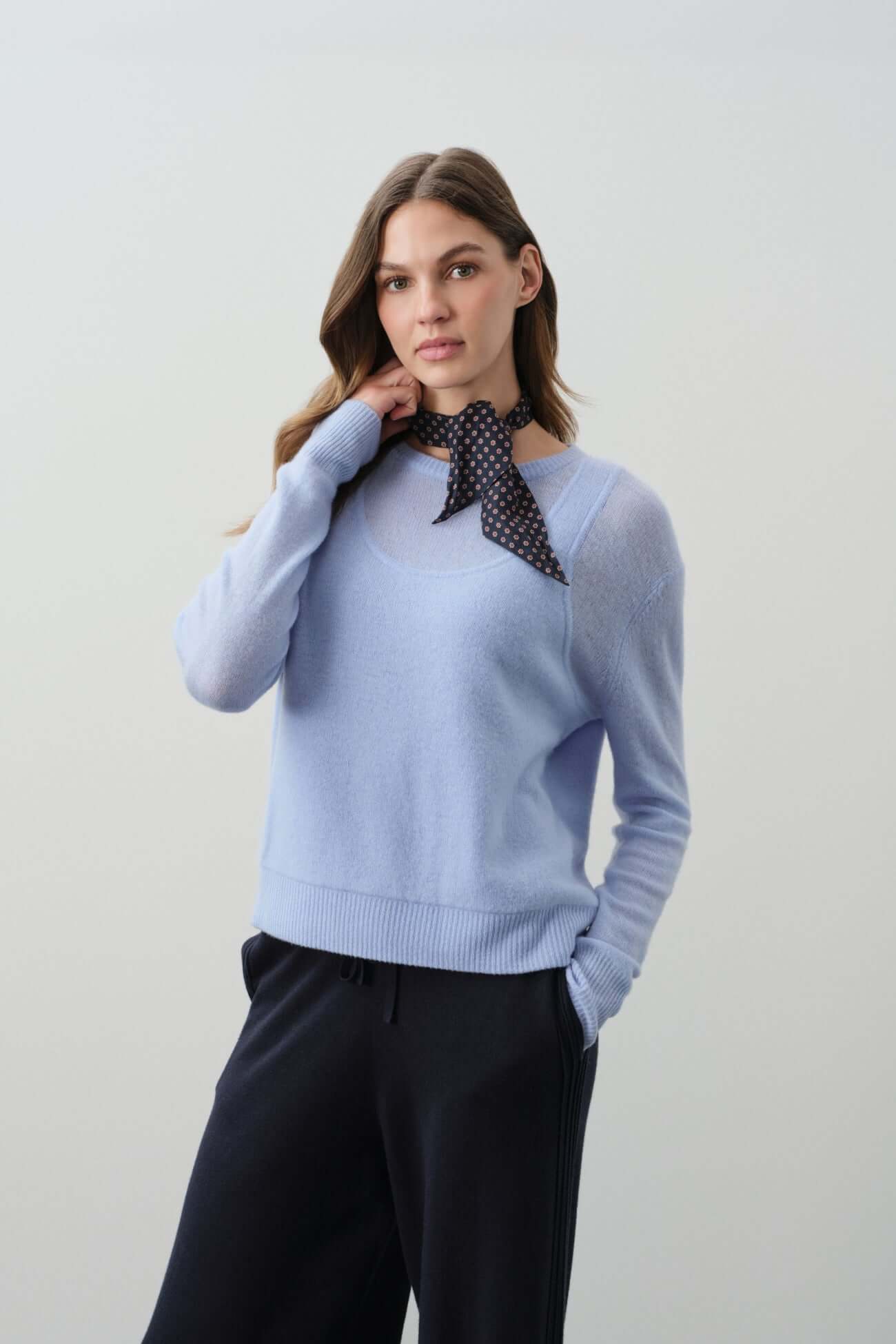 Model wearing a light blue sweater with a black polka dot scarf, showcasing elegant sweater styles.
